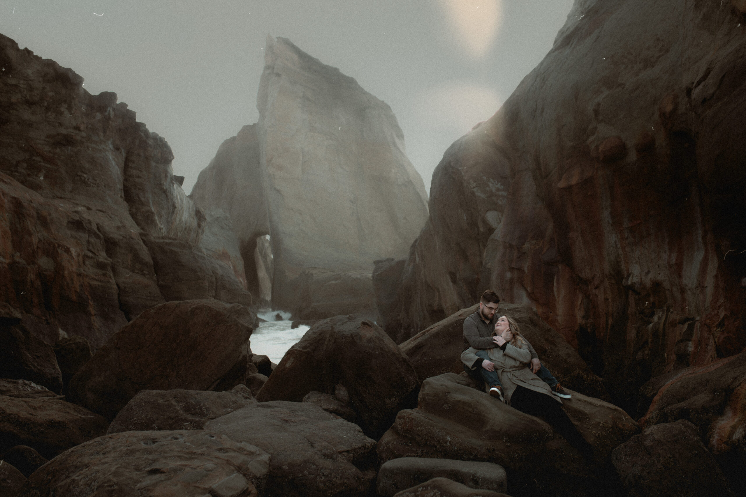 A couple sitting on a huge rock on the rocky shore of the Oregon Coast on an overcast day