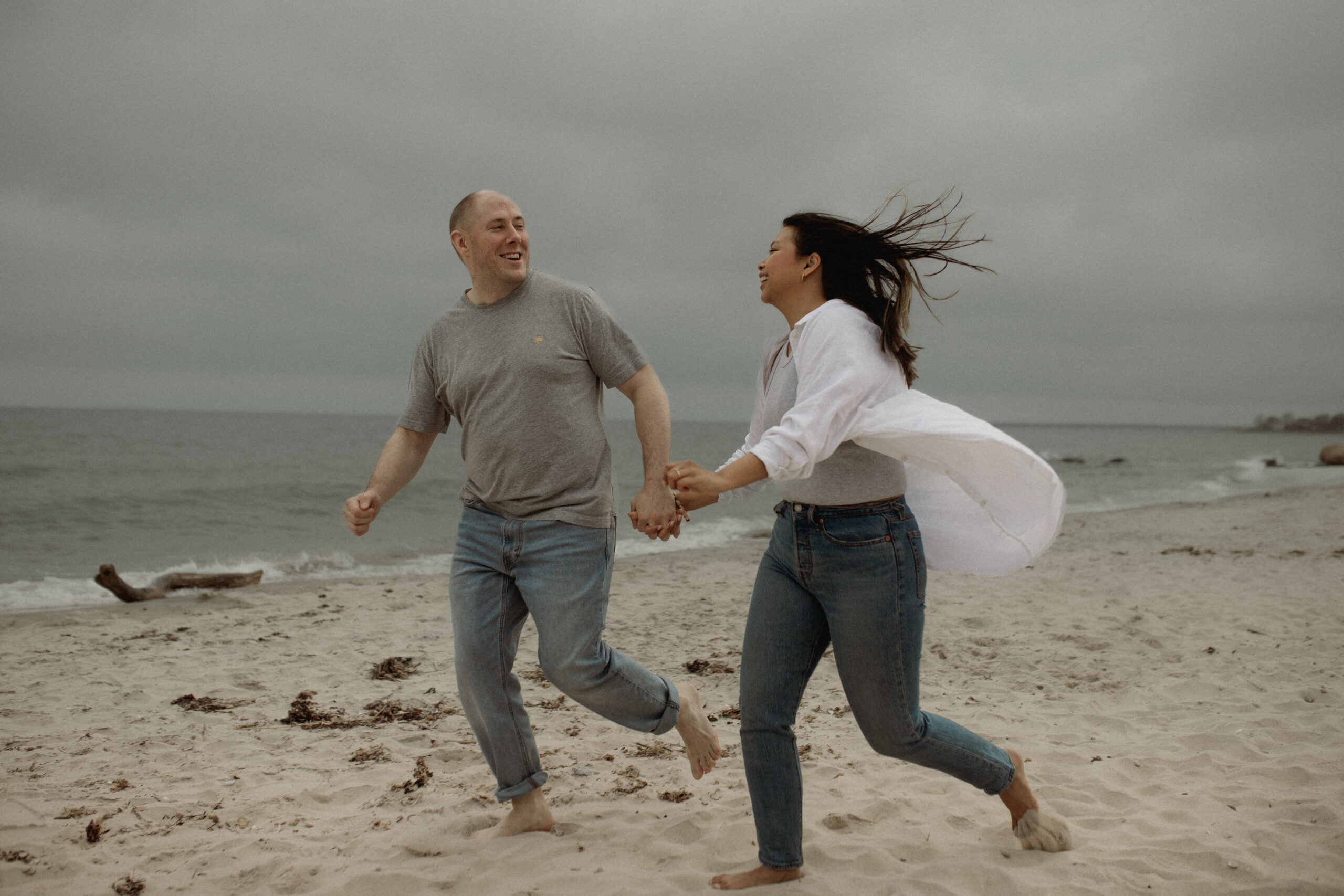 An engaged man and woman run down the beach holding hands during their photography session