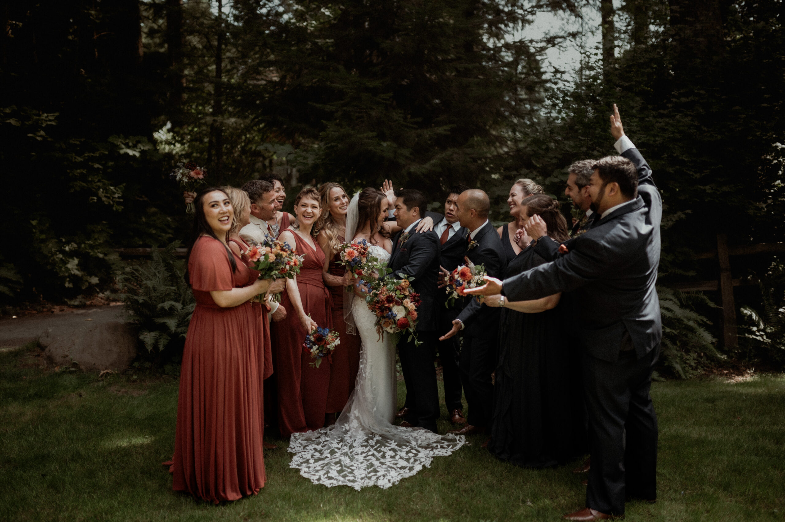 a wedding party around a bride and groom, with everyone cheering as the bride and groom kiss